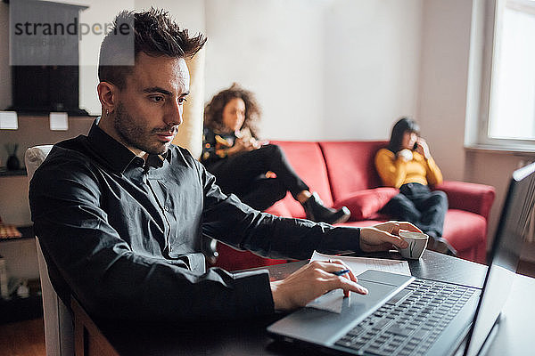 Mann am Laptop  Freunde entspannen sich im Hintergrund im Home-Office