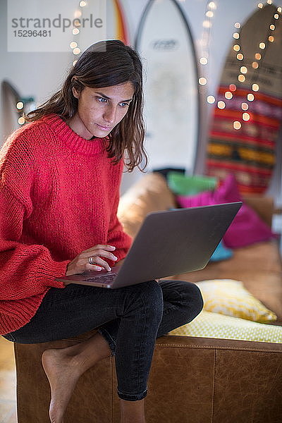 Junge Frau in rotem Pullover auf Wohnzimmer-Sofa mit Blick auf Laptop