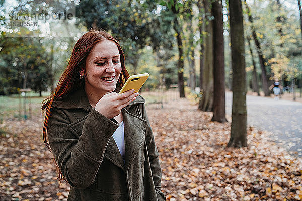 Junge Frau mit langen roten Haaren beim Smartphone-Selfie im Herbstpark