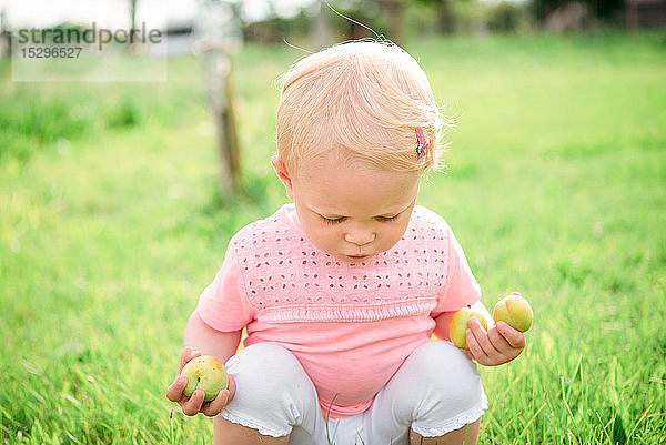 Süßes weibliches Kleinkind hockt auf Gras und schaut nach unten