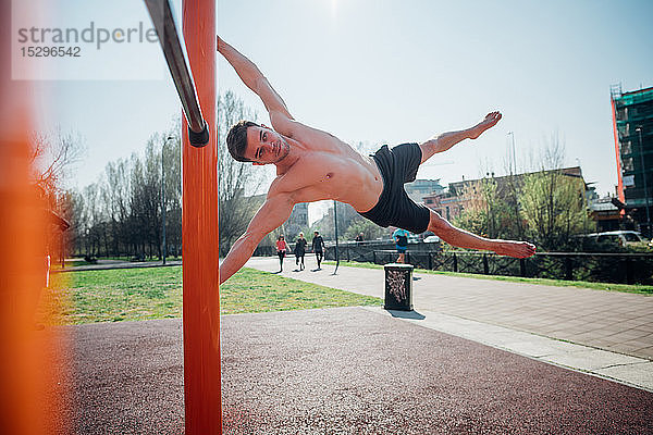 Gymnastik im Freien  junger Mann mit nacktem Oberkörper schwingt horizontal auf Übungsgeräten