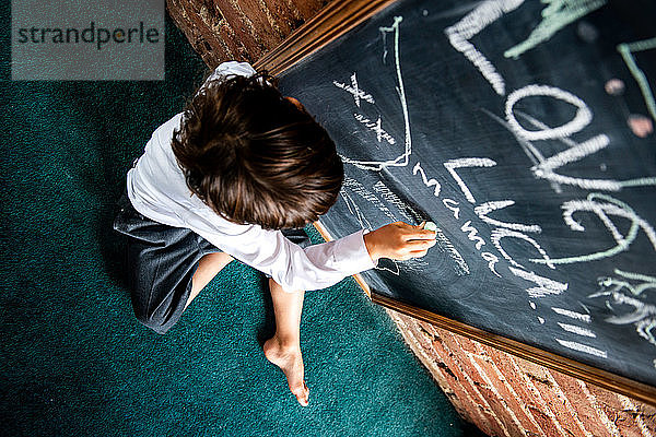 Junge in Schuluniform schreibt zu Hause an Tafel