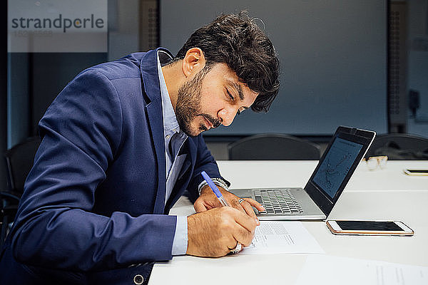 Geschäftsmann schreibt Notizen und benutzt Laptop im Büro