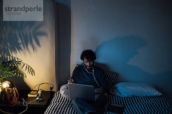 Bärtiger junger Mann mit Laptop im Bett