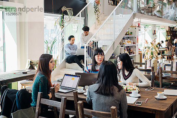 Junge Geschäftsfrauen  die an entfernten Arbeitsplätzen arbeiten und sich an einem Café-Tisch treffen