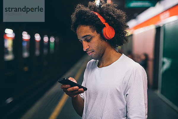 Junger Mann benutzt Smartphone auf Bahnsteig