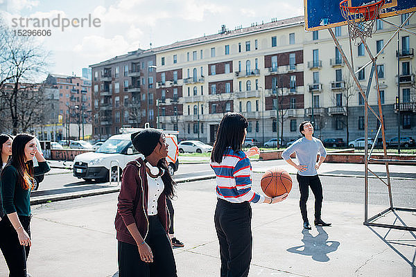 Junge weibliche und männliche erwachsene Freunde spielen Basketball auf dem Stadtplatz
