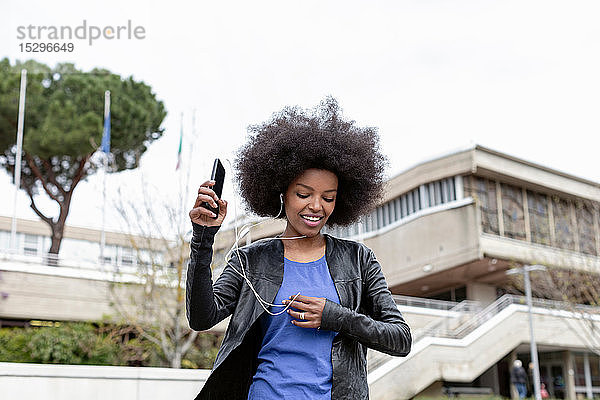 Junge Frau mit Afro-Haaren in der Stadt  die spazieren geht und Smartphone-Musik hört