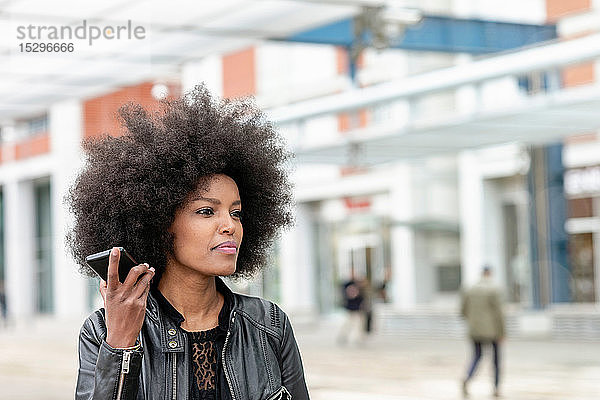 Junge Frau mit Afro-Haaren am Stadtbahnhof  die ein Smartphone hört