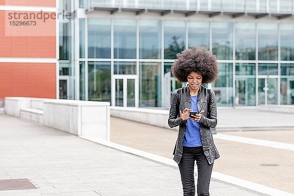 Junge Frau mit Afro-Haaren in der Stadt  die den Touchscreen eines Smartphones benutzt