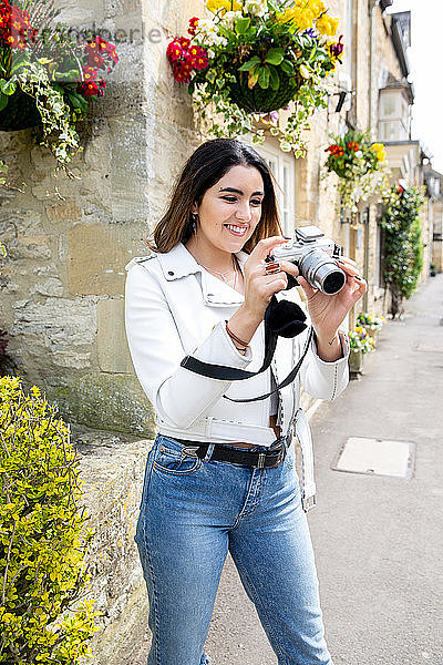 Junge Frau auf der Dorfstraße beim Betrachten von Fotos mit einer Digitalkamera  Cotswolds  England