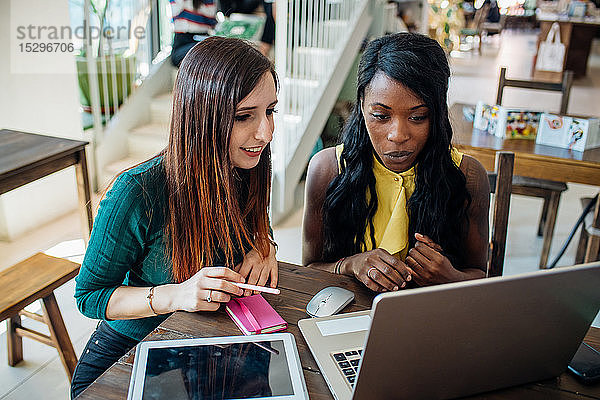 Junge Geschäftsfrauen arbeiten an entfernten Orten und schauen im Café auf den Laptop