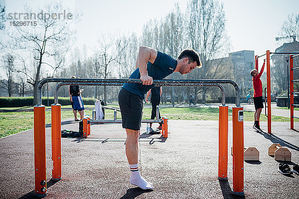 Gymnastik im Freien  junger Mann bereitet sich auf den Gebrauch von Barren vor  in voller Länge