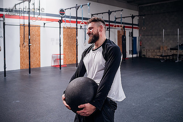 Junger Mann trainiert  hebt Atlasball im Fitnessstudio