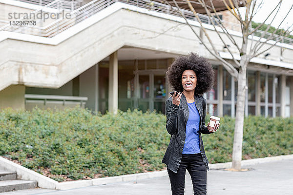 Junge Frau mit Afro-Haaren in der Stadt  geht zu Fuß und spricht mit Smartphone