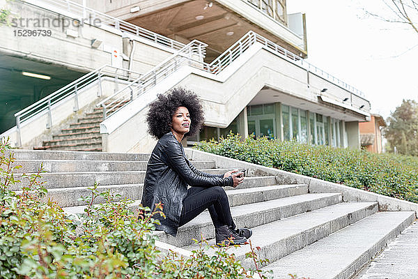 Junge Frau mit Afro-Haaren sitzt auf einer Stadttreppe und schaut weg