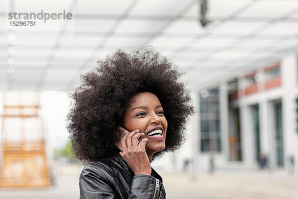 Junge Frau mit Afro-Haaren am Stadtbahnhof telefoniert mit einem Smartphone