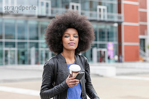 Junge Frau mit Afrofrisur in der Stadt  mit Smartphone und Kaffee zum Mitnehmen  Porträt