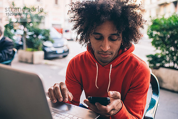 Junger Mann benutzt Smartphone und Laptop im Café