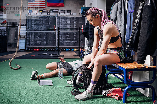 Junge Frau trainiert  sitzt auf Bank und packt Sporttasche im Fitnessstudio