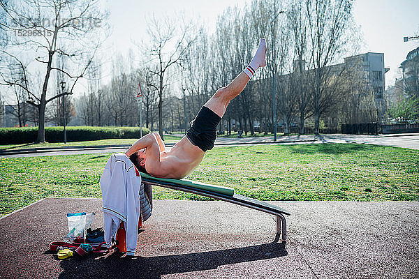 Gymnastik im Freien  junger Mann auf Hantelbank mit angehobenen Beinen