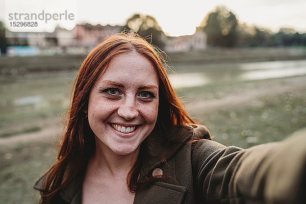 Junge Frau mit langen roten Haaren lächelt für Selbstgefälligkeit am Flussufer  persönliche Perspektive  Florenz  Toskana  Italien