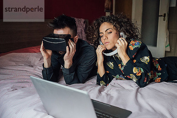 Paar mit VR-Headset und Laptop am Bett