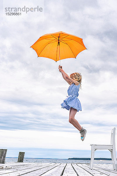 Mädchen wird mit einem Regenschirm von ihrem Stuhl gehoben