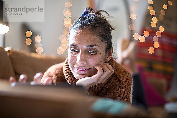 Junge Frau liegt auf dem Wohnzimmersofa und schaut auf den Laptop  Nahaufnahme