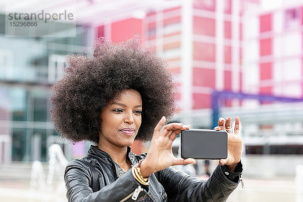 Junge Frau mit Afro-Haaren am Stadtbahnhof  nimmt Smartphone-Selfie