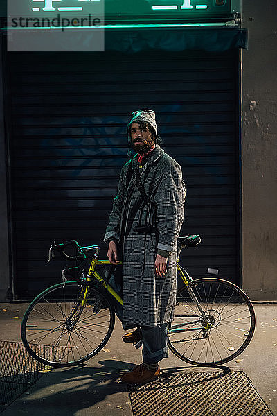 Bärtiger junger Mann mit Fahrrad auf dem Bürgersteig