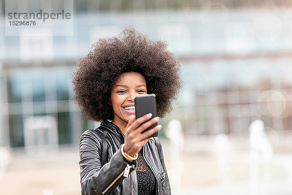 Junge Frau mit Afro-Haaren nimmt Smartphone-Selfie in der Stadthalle