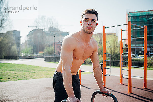 Gymnastik im Freien  junger Mann mit nacktem Oberkörper  der sich auf die Benutzung von Fitnessgeräten vorbereitet