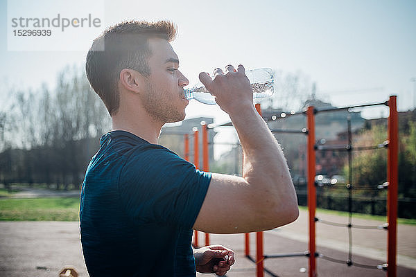 Gymnastik im Fitnessstudio im Freien  junger Mann trinkt Wasser in Flaschen