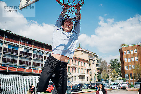Junger Mann hängt am Basketballkorb am städtischen Basketballplatz