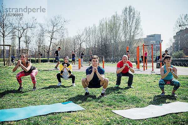 Gymnastikkurs im Freien  Frauen und Männer üben Yoga in Hockstellung