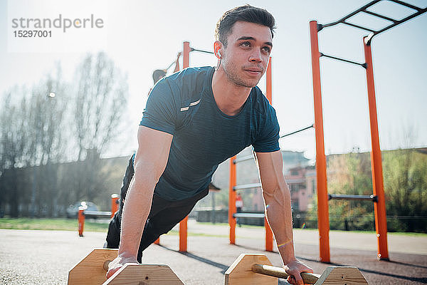 Gymnastik im Freien  junger Mann macht Liegestütze an Fitnessgeräten