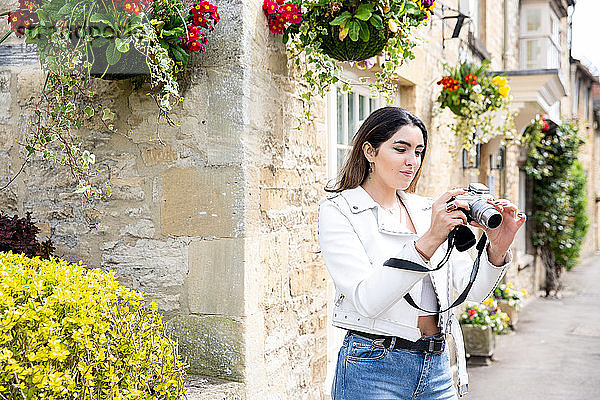 Junge Frau auf der Dorfstraße beim Betrachten von Fotos mit einer Digitalkamera  Cotswolds  England