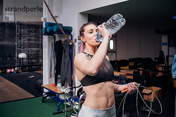 Junge Frau trainiert  trinkt Flaschenwasser im Fitnessstudio