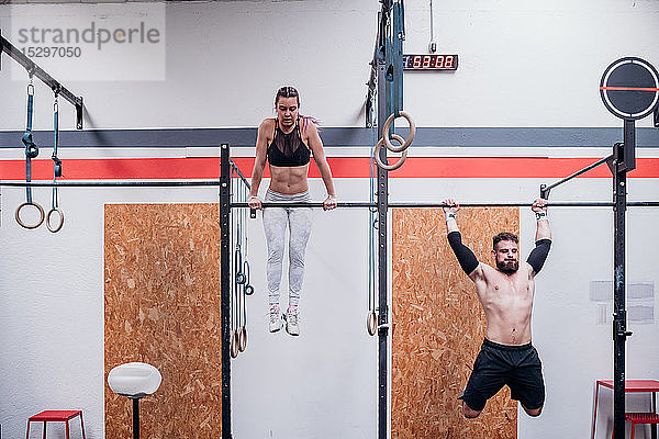 Junge Frau und Mann trainieren zusammen  an Übungsstangen im Fitnessstudio