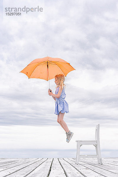 Mädchen wird mit einem Regenschirm von ihrem Stuhl gehoben