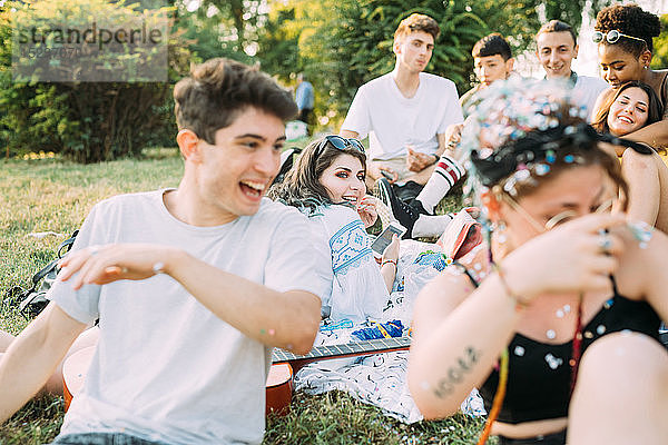 Gruppe von Freunden beobachtet Mann beim Picknick im Park  der mit Konfetti spielt