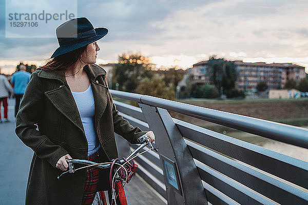 Junge Frau mit Fahrrad  die in der Abenddämmerung vom Steg aus den Blick auf sich zieht  Florenz  Toskana  Italien