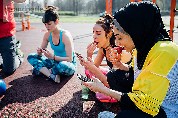Calisthenics-Kurs im Fitnessstudio im Freien  junge Frauen sitzen  schauen auf Smartphones und essen Obst