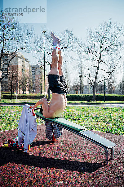 Gymnastik im Freien  junger Mann kopfüber auf der Hantelbank