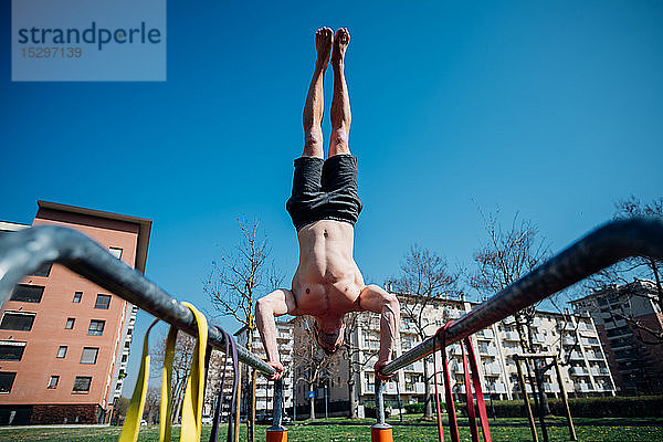 Gymnastik im Freien  junger Mann mit nacktem Oberkörper beim Handstand am Barren  Blickwinkel niedrig