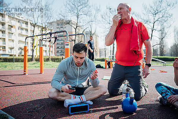 Calisthenics-Kurs im Fitnessstudio im Freien  Männer sitzen vor einem Smartphone und essen Obst