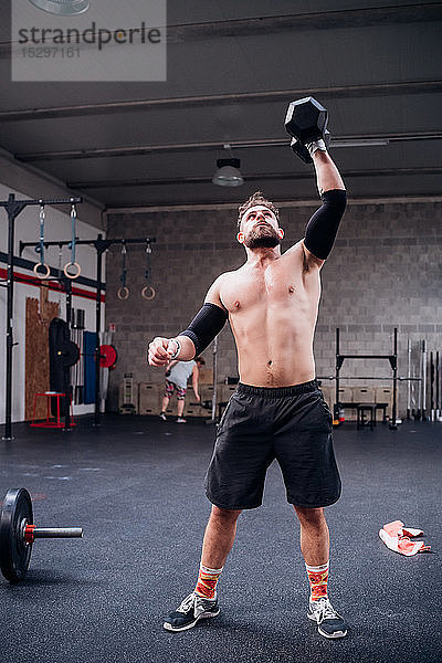 Training eines jungen Mannes mit nacktem Oberkörper  Heben einer Hantel im Fitnessstudio