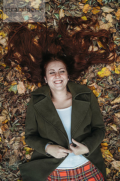 Junge Frau mit langen roten Haaren liegt lachend im Herbstlaub  Blick von oben