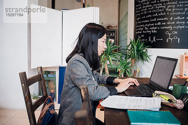 Junge Geschäftsfrau arbeitet ferngesteuert am Laptop am Cafétisch